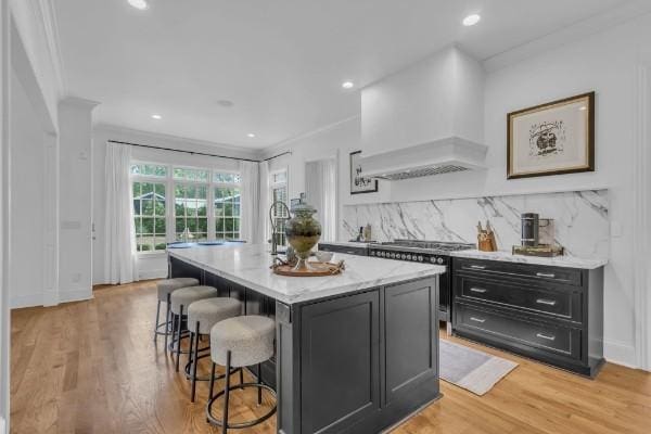 kitchen with premium range hood, a kitchen bar, tasteful backsplash, a center island with sink, and ornamental molding