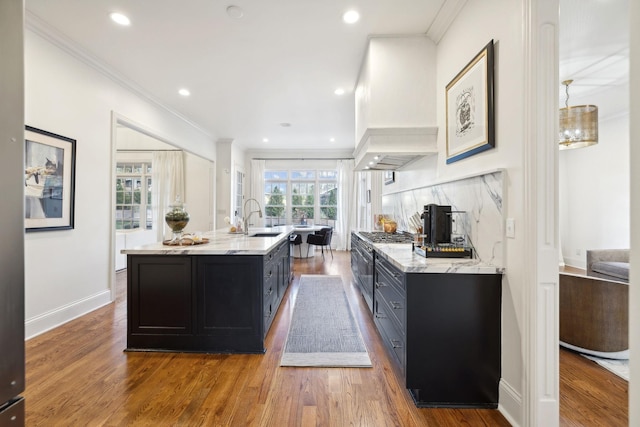 kitchen featuring sink, hardwood / wood-style flooring, high end stainless steel range oven, premium range hood, and a center island with sink