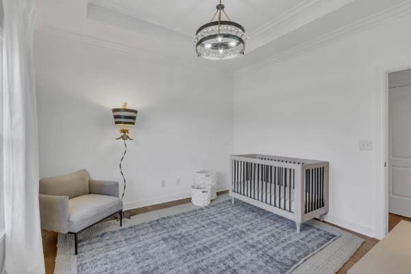 bedroom with a raised ceiling, ornamental molding, a nursery area, and a notable chandelier