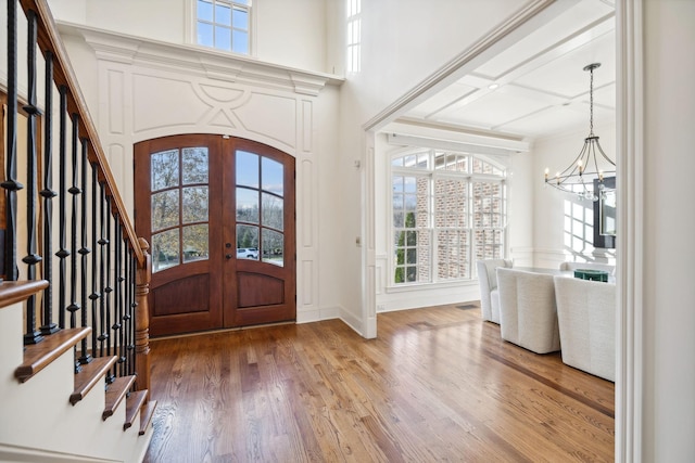 foyer entrance featuring french doors, wood-type flooring, an inviting chandelier, and a high ceiling