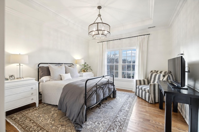 bedroom featuring hardwood / wood-style flooring, crown molding, a notable chandelier, and a tray ceiling