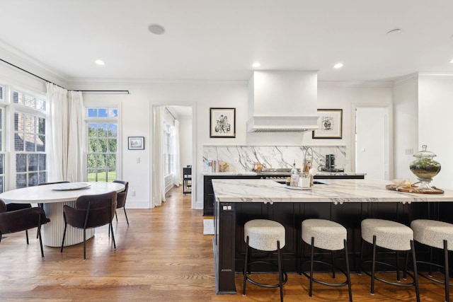 kitchen with premium range hood, light stone countertops, a breakfast bar area, and decorative backsplash