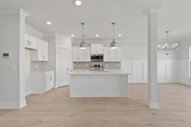 kitchen with decorative light fixtures, an island with sink, stainless steel appliances, light hardwood / wood-style floors, and white cabinets