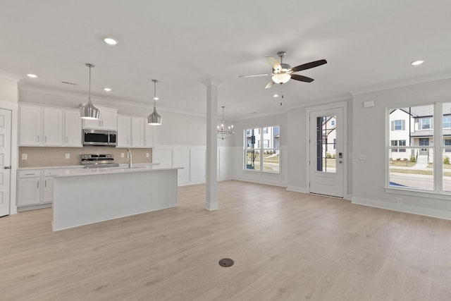 kitchen with white cabinetry, hanging light fixtures, ornamental molding, an island with sink, and stainless steel appliances