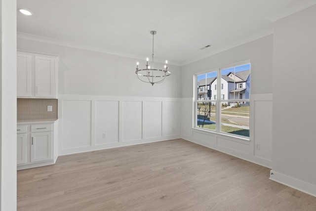 unfurnished dining area featuring crown molding, a chandelier, and light hardwood / wood-style floors