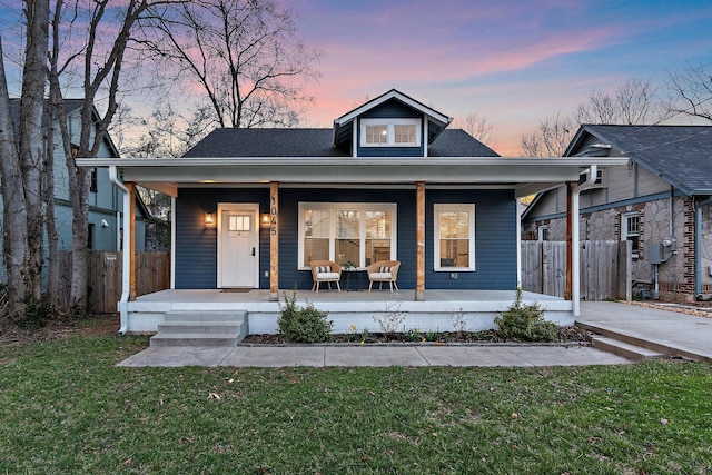 bungalow-style house with covered porch, a lawn, and fence