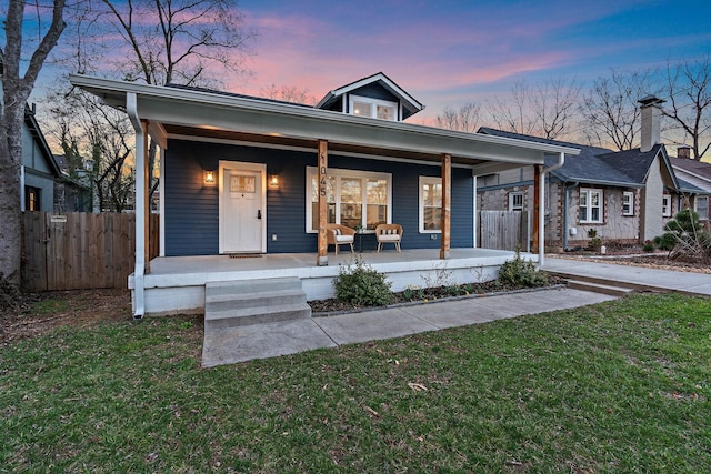 bungalow-style house with covered porch, fence, and a lawn