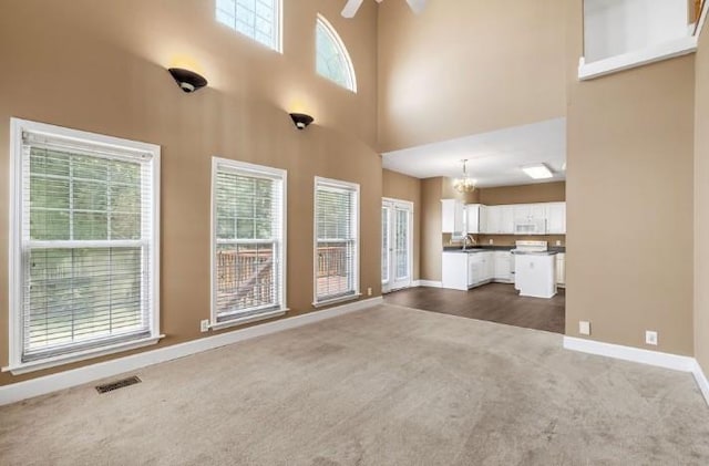 unfurnished living room featuring a high ceiling, dark colored carpet, sink, and ceiling fan