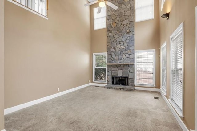 unfurnished living room with a stone fireplace, a towering ceiling, ceiling fan, and carpet