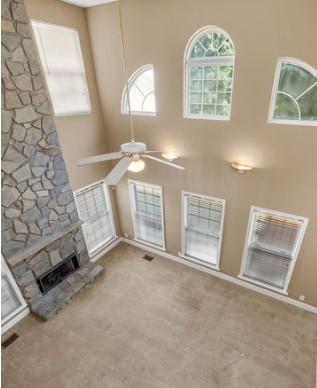 unfurnished living room featuring a stone fireplace, carpet floors, ceiling fan, and a towering ceiling