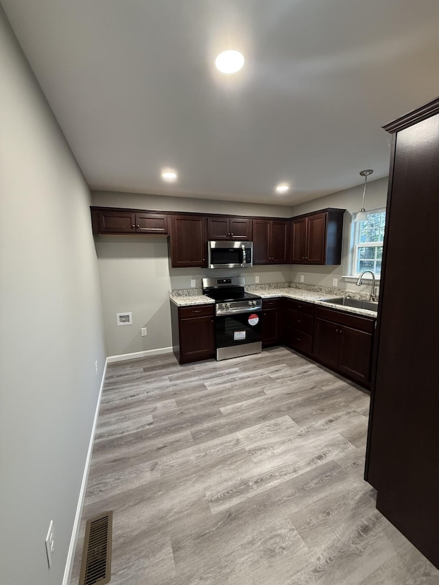 kitchen featuring appliances with stainless steel finishes, pendant lighting, sink, light hardwood / wood-style floors, and dark brown cabinets