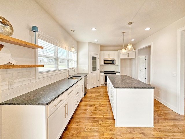 kitchen with a kitchen island, sink, white cabinets, hanging light fixtures, and stainless steel appliances