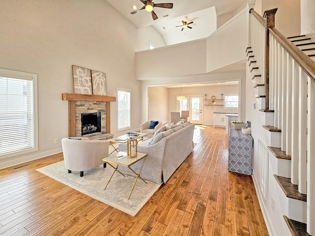 living room featuring hardwood / wood-style flooring, a stone fireplace, high vaulted ceiling, and ceiling fan