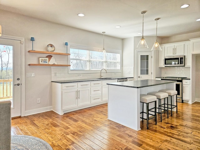 kitchen with appliances with stainless steel finishes, decorative light fixtures, white cabinetry, a breakfast bar area, and light wood-type flooring