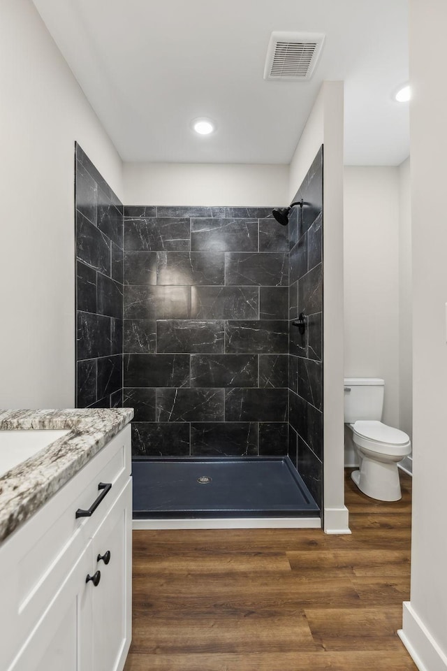 bathroom with vanity, hardwood / wood-style floors, toilet, and tiled shower