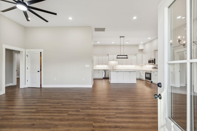 unfurnished living room featuring ceiling fan with notable chandelier, dark hardwood / wood-style floors, and a high ceiling