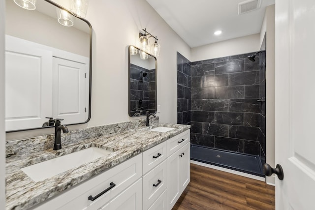 bathroom with wood-type flooring, a tile shower, and vanity