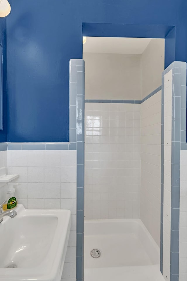 bathroom with a tile shower, sink, and tile walls