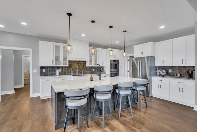 kitchen featuring dark hardwood / wood-style floors, decorative light fixtures, an island with sink, white cabinets, and stainless steel appliances