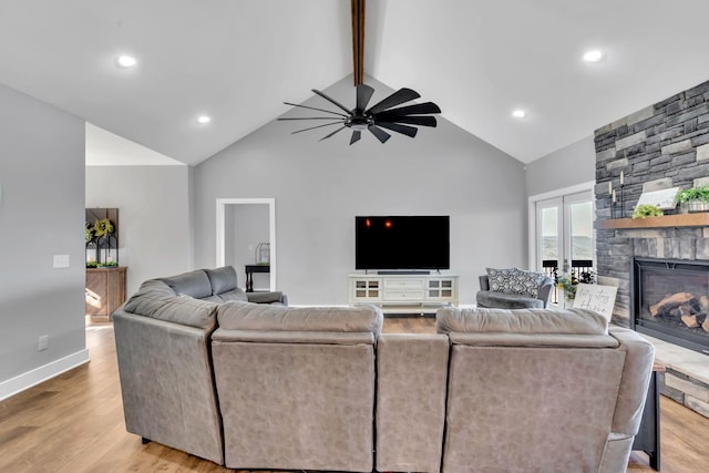 living room featuring high vaulted ceiling, a fireplace, ceiling fan, light hardwood / wood-style floors, and beam ceiling