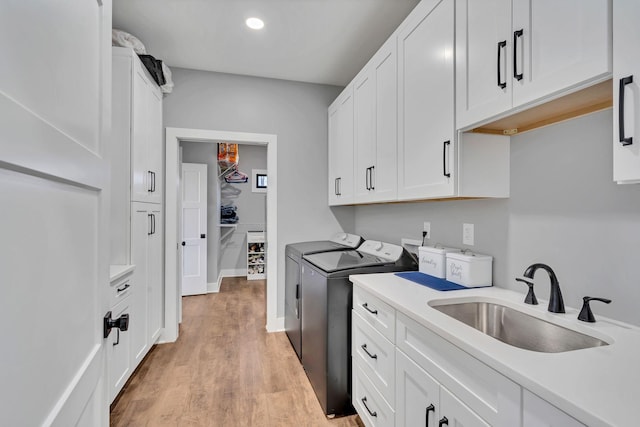 laundry area with separate washer and dryer, sink, light hardwood / wood-style floors, and cabinets