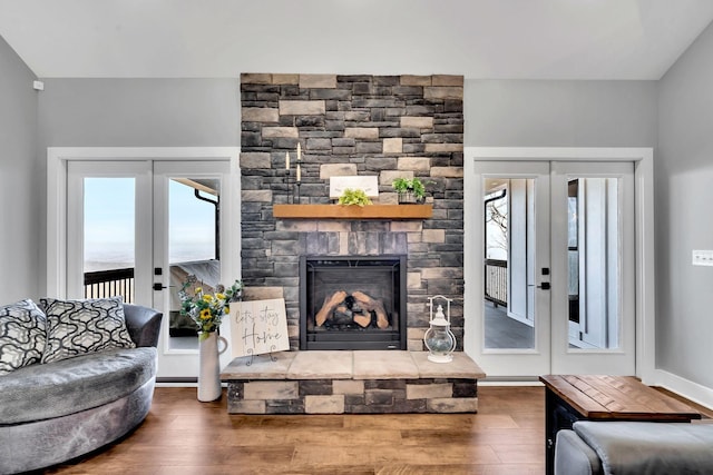 living room featuring hardwood / wood-style floors, a stone fireplace, vaulted ceiling, and french doors