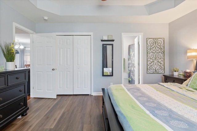 bedroom with ensuite bath, dark wood-type flooring, a closet, and a raised ceiling