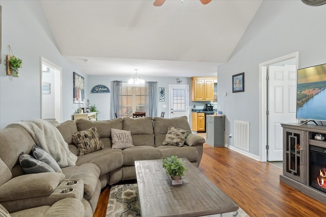 living room featuring dark wood-type flooring, ceiling fan with notable chandelier, and high vaulted ceiling