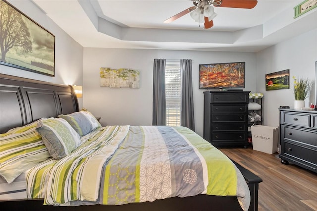 bedroom with ceiling fan, dark hardwood / wood-style floors, and a raised ceiling