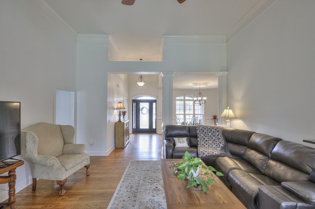 living room with ceiling fan with notable chandelier, ornamental molding, decorative columns, and light wood-type flooring