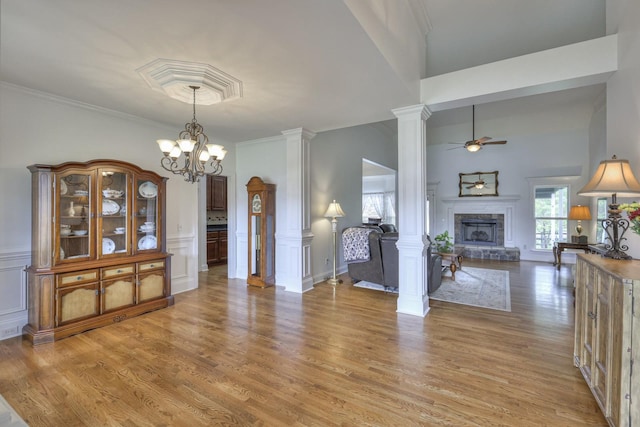 dining space featuring crown molding, decorative columns, a fireplace, light hardwood / wood-style floors, and ceiling fan with notable chandelier