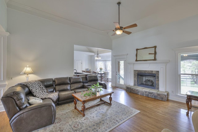 living room featuring ceiling fan with notable chandelier, a stone fireplace, hardwood / wood-style floors, and high vaulted ceiling