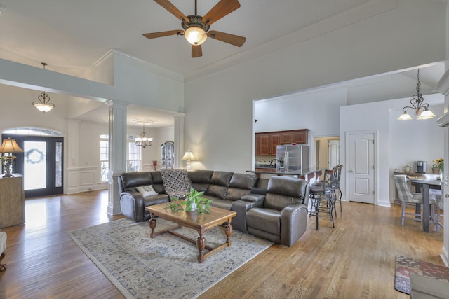 living room featuring crown molding, a towering ceiling, decorative columns, and light hardwood / wood-style floors