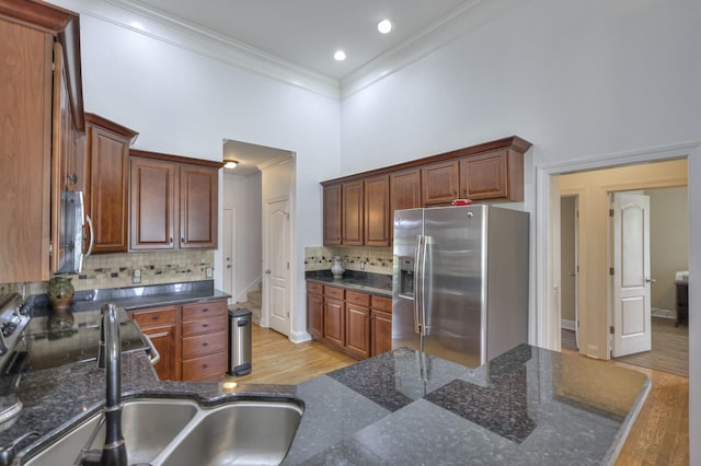 kitchen with sink, dark stone countertops, a towering ceiling, stainless steel appliances, and light hardwood / wood-style floors