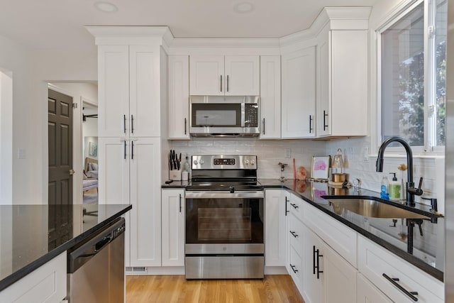 kitchen with sink, appliances with stainless steel finishes, white cabinetry, dark stone counters, and light wood-type flooring