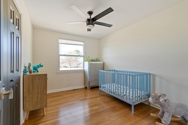 bedroom featuring a crib, ceiling fan, and light hardwood / wood-style floors