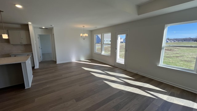 unfurnished living room featuring an inviting chandelier, plenty of natural light, and dark hardwood / wood-style floors