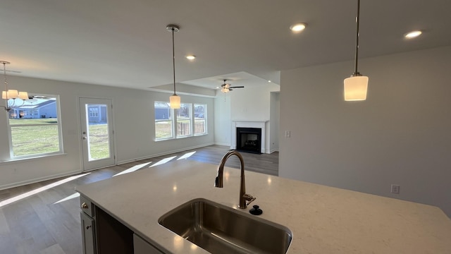 kitchen with pendant lighting, dark hardwood / wood-style flooring, light stone countertops, and sink