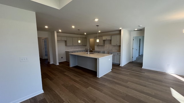 kitchen with an island with sink, sink, decorative backsplash, hanging light fixtures, and dark wood-type flooring