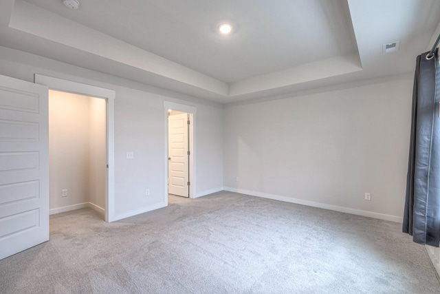 unfurnished bedroom featuring a raised ceiling and light carpet