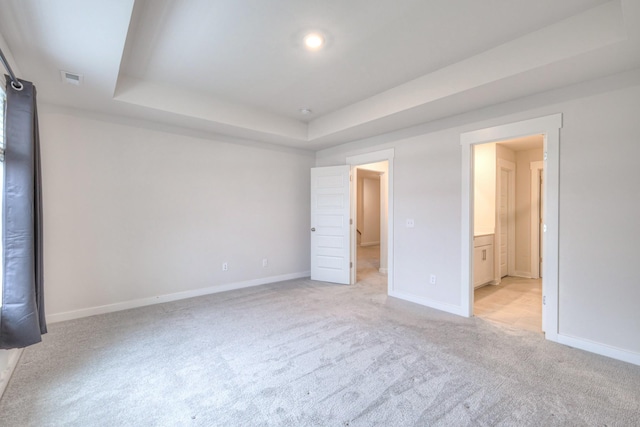 unfurnished bedroom with a tray ceiling, ensuite bath, and light colored carpet