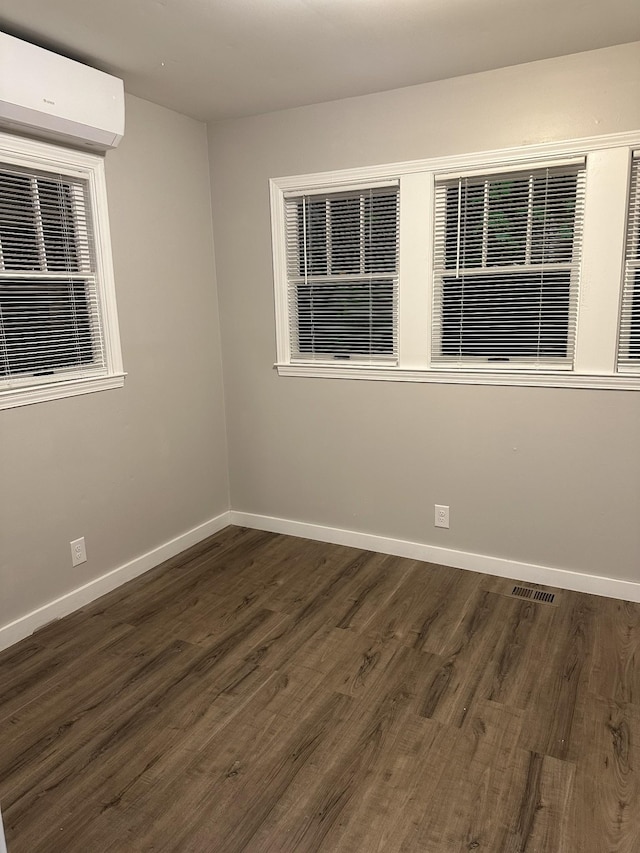 unfurnished room featuring a wall mounted air conditioner and dark hardwood / wood-style flooring