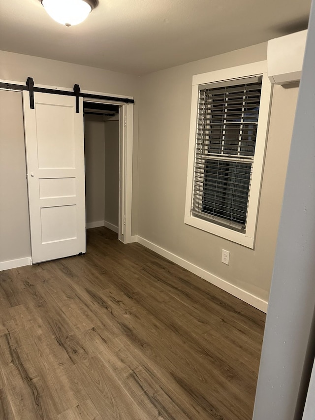 unfurnished bedroom with a closet, dark hardwood / wood-style floors, and a barn door