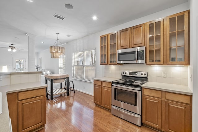 kitchen featuring pendant lighting, stainless steel appliances, tasteful backsplash, ceiling fan with notable chandelier, and light wood-type flooring