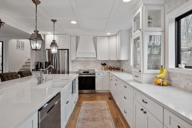 kitchen featuring premium range hood, white cabinetry, decorative light fixtures, appliances with stainless steel finishes, and light hardwood / wood-style floors