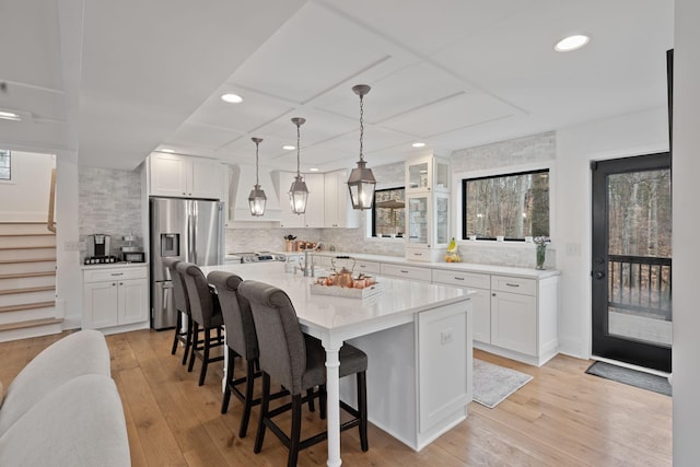 kitchen with white cabinets, a center island with sink, stainless steel fridge, and a kitchen breakfast bar