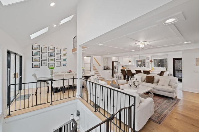 living room with an inviting chandelier, a skylight, high vaulted ceiling, and light hardwood / wood-style flooring