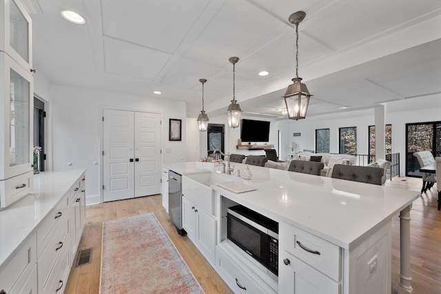 kitchen featuring a breakfast bar, appliances with stainless steel finishes, an island with sink, pendant lighting, and white cabinets