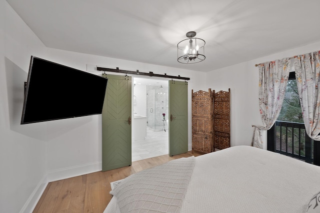 bedroom with ensuite bathroom, a barn door, a chandelier, and light hardwood / wood-style flooring