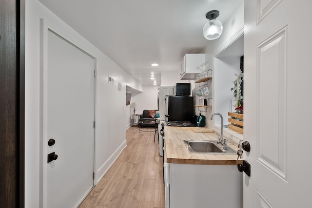 kitchen with wooden counters, light hardwood / wood-style floors, sink, and white cabinets